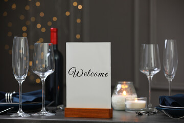 Holder with word Welcome on table set for couple in restaurant