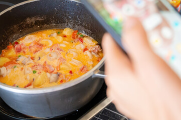 Seafood soup. A woman's hand holds a phone over the stove, filming the finished dish.