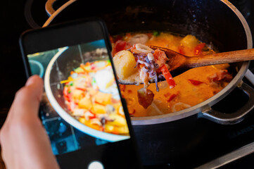 Seafood soup. A woman's hand holds a phone over the stove, filming the finished dish.