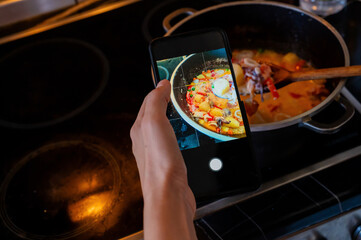Seafood soup. A woman's hand holds a phone over the stove, filming the finished dish.