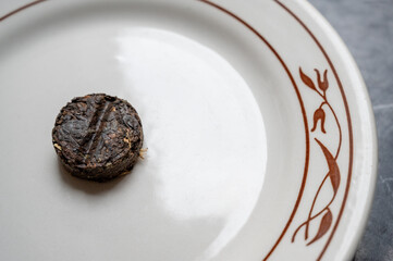 Compressed Pu-erh tea cake resting on a ceramic plate. The earthy texture and deep brown tones of the tea tablet contrast with the clean surface, emphasizing traditional tea culture and minimalism.