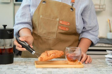 Senior entrepreneur cafe owner barista presents bakery croissants on tray, Asian retired female in apron grins across counter, grinder and shelves create welcoming small business hospitality scene