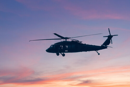 A silhouette of a military helicopter flying against a bright blue sky, showcasing its structure and movement during an airborne operation.