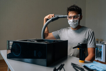 Computer technician wearing face mask and safety glasses puts vacuum cleaner to head, during cleaning computer case with vacuum cleaner, ensuring proper functioning and preventing overheating.