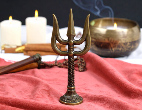 A bronze Shiva trident on a velvet cloth, lit by warm candlelight, with subtle smoke swirls, vivid detail