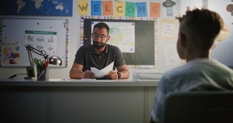 Male Teacher Presenting School Exam Results to Primary School Boy, Discussing Poor Performance, Low Grades and Behavior with Student. Extracurricular Meeting to Support Child's Learning. Dolly Shot.