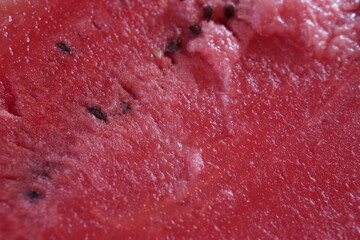 Macro shot of fresh, juicy watermelon pulp with visible seeds. The vibrant red color and textured surface of the fruit are highlighted