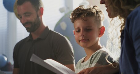 Mother and Father Looking at School Test Results of Their Son During Parents Evening. Parents Happy About Excellent Academic Performance and Behavior of Elementary School Boy. Slow Motion. Close Up.