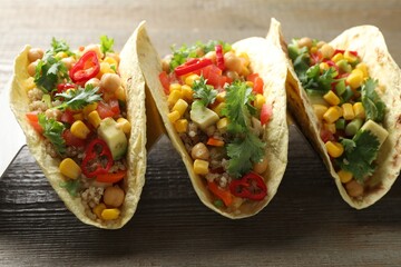 Tasty vegetarian tacos with chickpeas, corn and quinoa served on wooden table, closeup