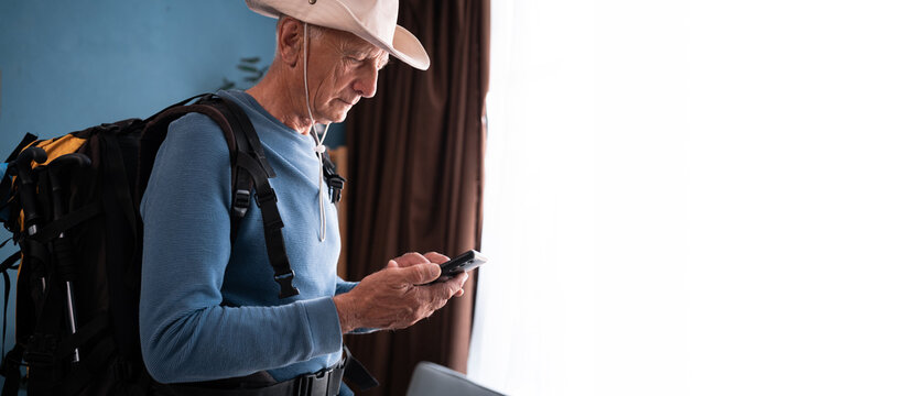 Elderly man hiker using smartphone at home preparing to hike trip