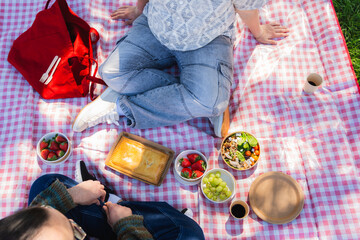 Two people enjoying a romantic picnic outdoors, sharing food and drinks on a checkered blanket