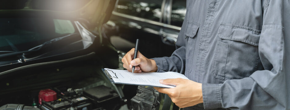 Auto check up and car service shop concept. Mechanic writing job checklist to clipboard to estimate repair quotation to client at workshop garage.