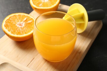 Fresh orange juice in glass, fruits and juicer on black table, closeup