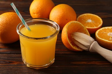 Fresh orange juice in glass, fruits and juicer on wooden table, closeup