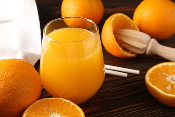 Fresh orange juice in glass, fruits, straws and juicer on wooden table, closeup
