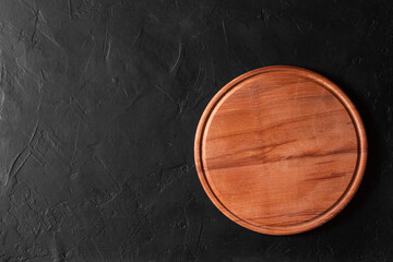 Round wooden cutting board on black background.