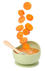 Baby food. Carrot slices falling into bowl of puree on white background