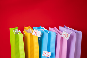 Multi colored shopping bags, with various discount percentage tags on a red background, sale shopping concept