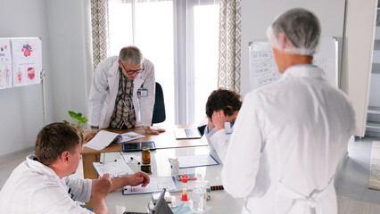 A medical error. The head physician of the clinic chastises his subordinate for harming the patient. A group of doctors gathered around a table