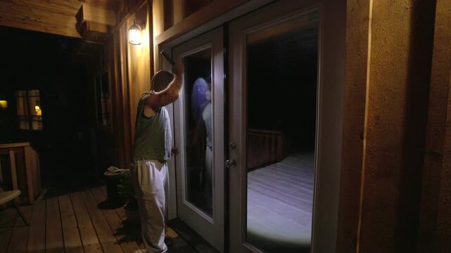 masked man holding a crowbar and looking into a home through window blinds at night. The unsettling atmosphere evokes fear and suspense, ideal for illustrating concepts of crime, danger, home invasion
