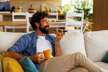 Happy freelancer using smartphone for business recording voice message and drinking coffee, working from home