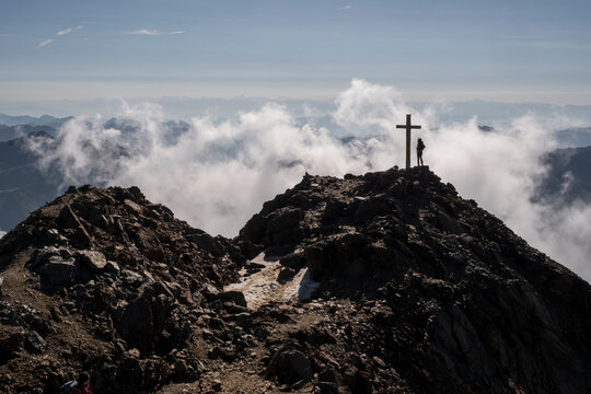Vioz peak with a cross and a person silhouetted against a cloudy sky. The refuge Mantova al Vioz is a starting point for climbing the Vioz peak.