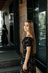 A woman in a dress stands against a wooden wall.