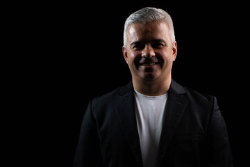 Fototapeta premium Smiling businessman standing confidently under chiaroscuro lighting, professional studio portrait on dark background