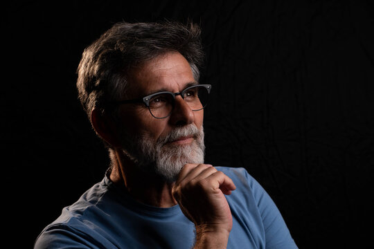 Mature man posing under chiaroscuro light with positive yet mysterious gaze, dramatic portrait in low key lighting