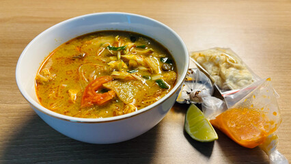 Traditional Indonesian Soto Ayam soup in a white bowl with lime chili sauce and crackers.