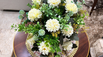 Artificial bouquet of cream chrysanthemums and lush greenery on a decorative wooden table.