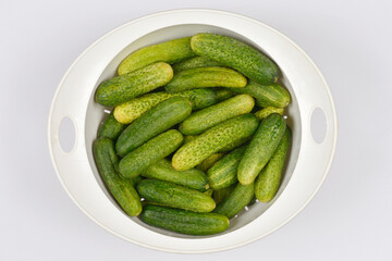 An overhead view of a plastic bowl filled with fresh pickling cucumbers