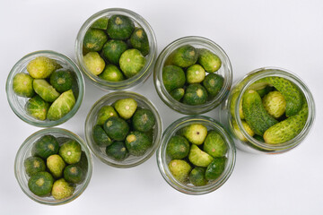 Multiple open glass jars filled with fresh cucumbers, being prepared for pickling or preserving on a white background