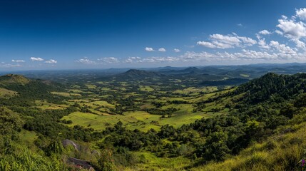 Fototapeta premium Panoramic vista of a valley nestled between hills. Lush green valleys and forests stretch out below, contrasting with a backdrop of distant mountain ranges. 