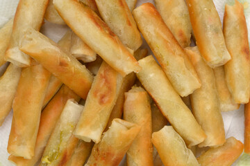 A high-angle close-up shot of a pile of freshly fried spring rolls draining on a paper towel