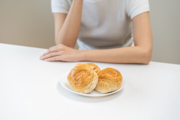 Gluten allergy, asian young woman, girl refusing to eat, looking at bread slice on plate in breakfast food meal on table at home, having a stomach ache. Gluten intolerant and Gluten free diet concept.