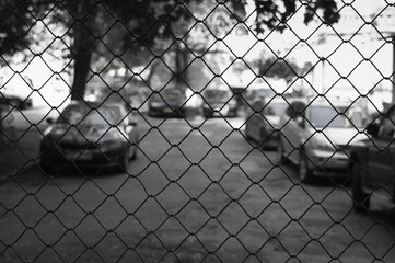gray background, in the photo there is a chain-link fence, in the background there is a road and cars