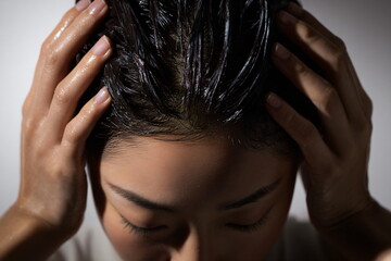 Naklejka premium Woman applying conditioner on wet dark hair. Hair care, treatment, and beauty routine. Skincare, health, hygiene concept.