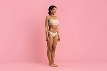 Smiling young African American woman in stylish beige underwear standing in studio on pink background, joyful and confident. Healthy and empowering fashion and body image visual, copy space