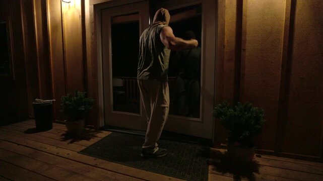 masked man holding a crowbar and looking into a home through window blinds at night. The unsettling atmosphere evokes fear and suspense, ideal for illustrating concepts of crime, danger, home invasion