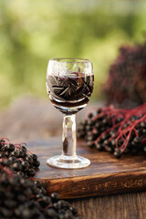 A shot glass of black elder syrup with fresh elderberries outdoors