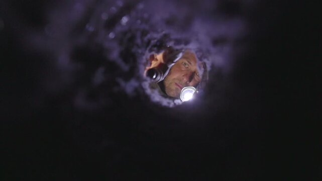 Man inspecting a dryer vent with a flashlight, checking for lint buildup and blockages. The image captures a real-life home maintenance moment, emphasizing fire prevention, appliance safety, and respo