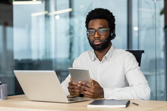 Focused man using tablet and laptop while on a call in a modern office. - Powered by Adobe