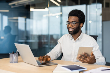 Professional man analyzing work on a laptop, multitasking with a tablet in his office.