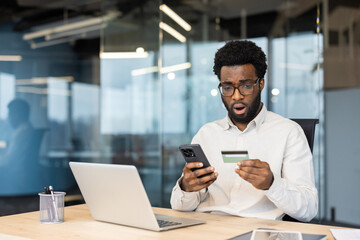 Professional man at a desk in a modern office, surprised by credit card details on his phone.