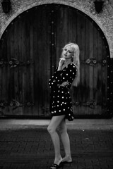 Naklejka premium Portrait of a beautiful blonde girl in a white polka dot dress outdoors. Black and white photo.
