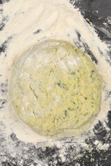 A ball of dough made from zucchini, cheese, and flour is dusted with flour on a dark surface, representing the preparation for gnocchi