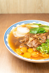 Top view of Asian beef noodle soup served in broth with fresh bok choy, daikon, carrots, and cilantro in a ceramic bowl on wooden table.