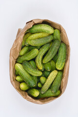 An overhead shot of a paper bag filled with fresh pickling cucumbers resting on a white surface