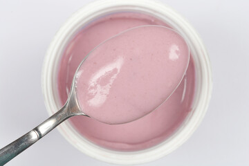 A spoonful of creamy fruit yogurt is lifted from a cup, highlighting its smooth texture and light purple color against a white background